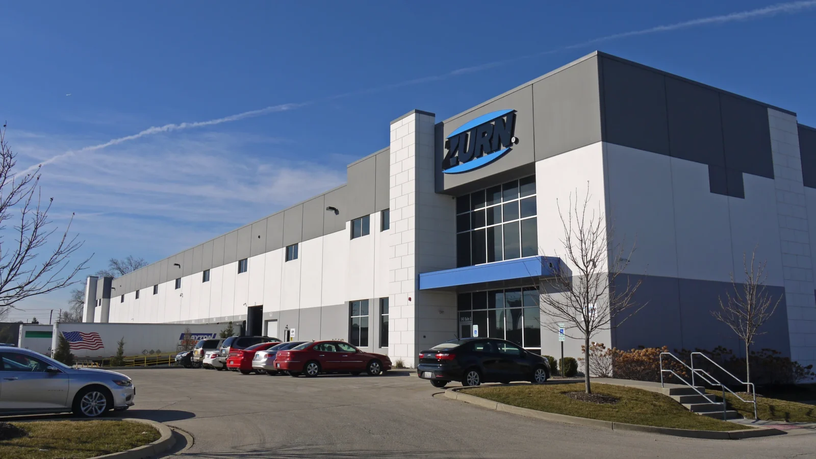 Zurn tenant entry with a tall glass bay, blue canopy and precast pilaster, the long white warehouse wall stretching back behind it.
