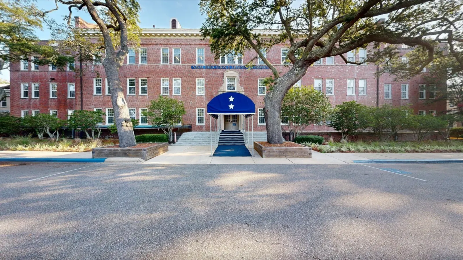 Street-level view from inside the same 3D scan: the brick building front with its blue entrance awning, framed by live oaks.