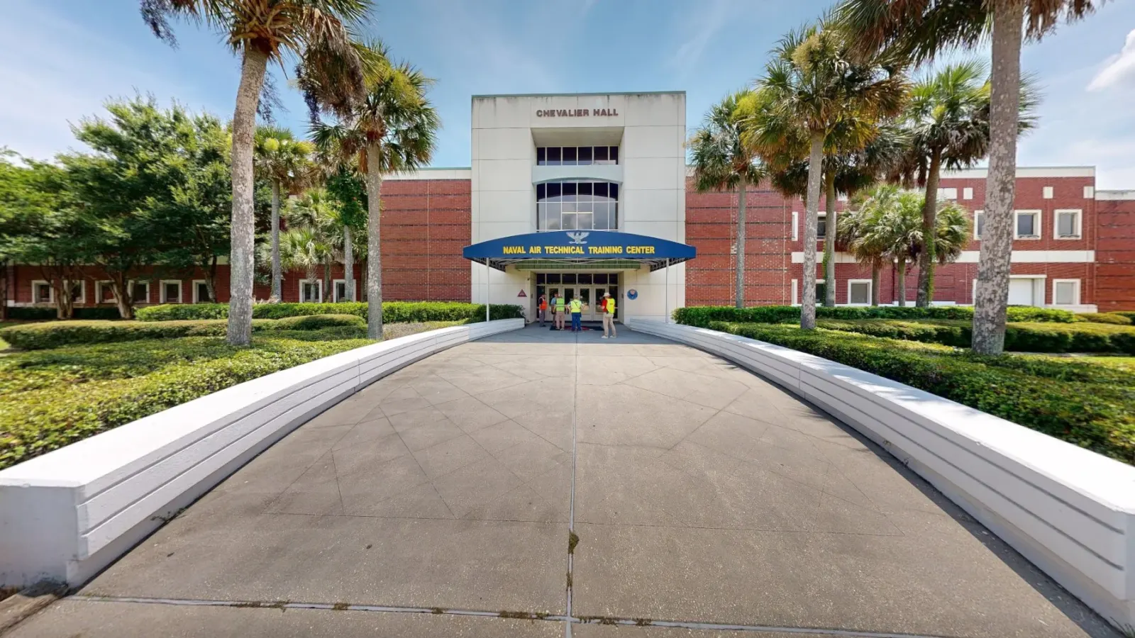 Street-level view from a 3D scan of a training center at NAS Pensacola: a walkway between low white walls leads to the canopied entrance, framed by palms.