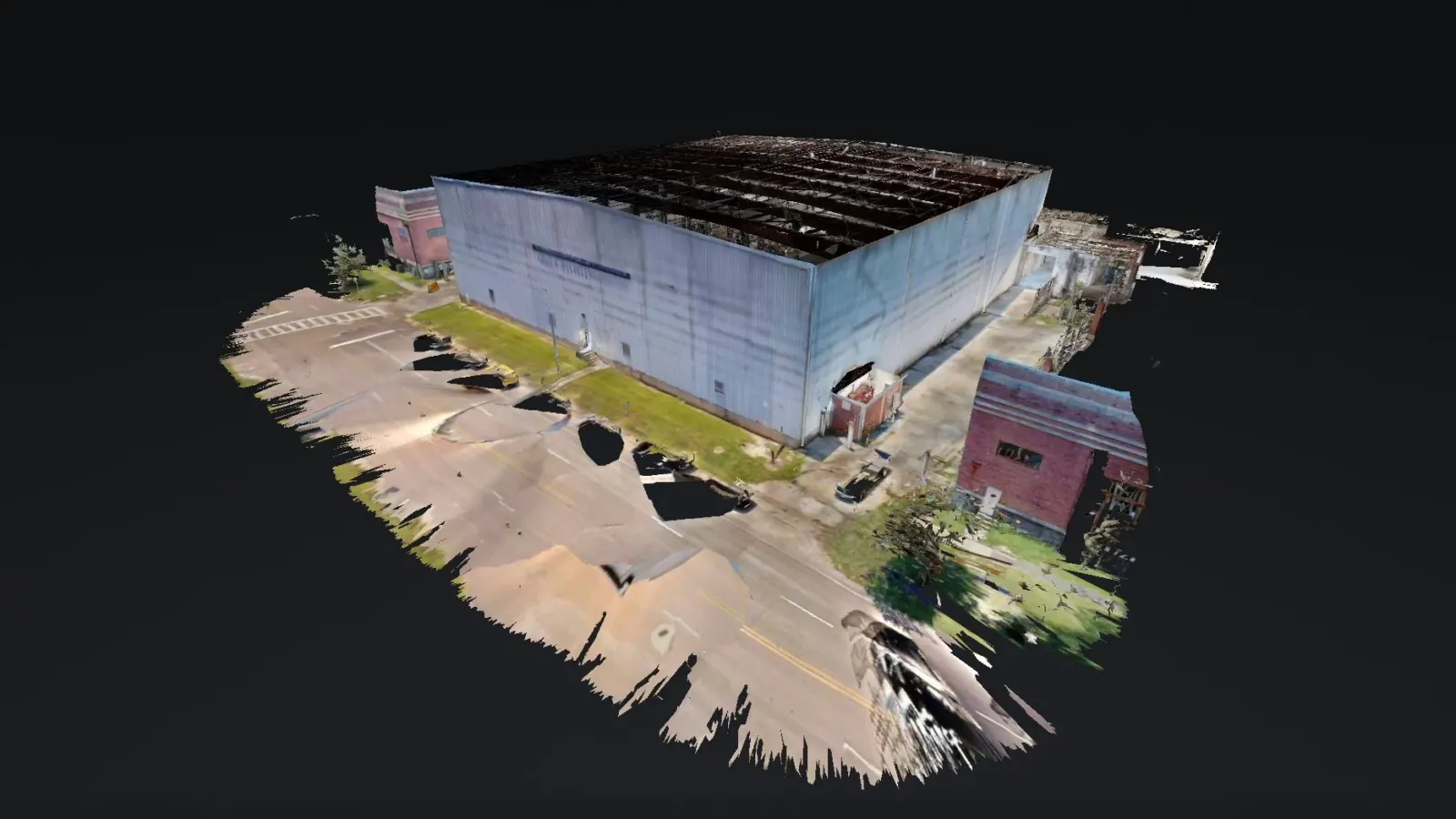 Dollhouse view of a 3D scan of a large metal-clad warehouse building at NAS Pensacola, with its parking lot and a neighboring brick building.