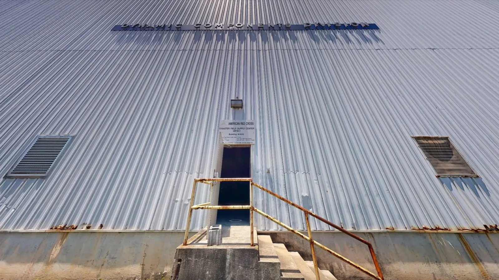 Street-level view from the same 3D scan: a corrugated metal wall with two louvers and a steel stair up to a single entry door.