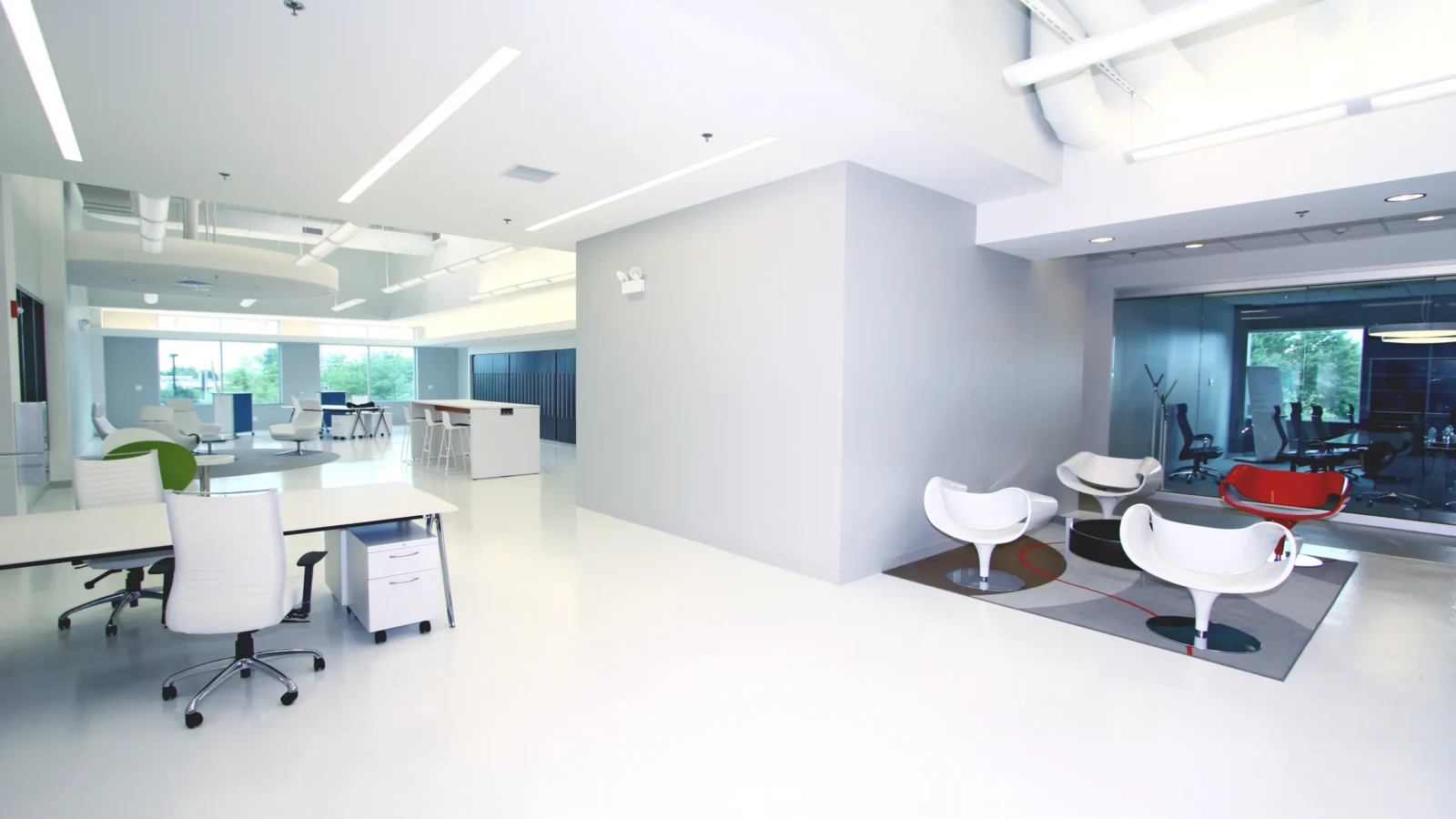 Clariant Colorworks' open design studio, white epoxy floors and white workstations with a lounge of sculptural white and red chairs and glass-walled conference room.