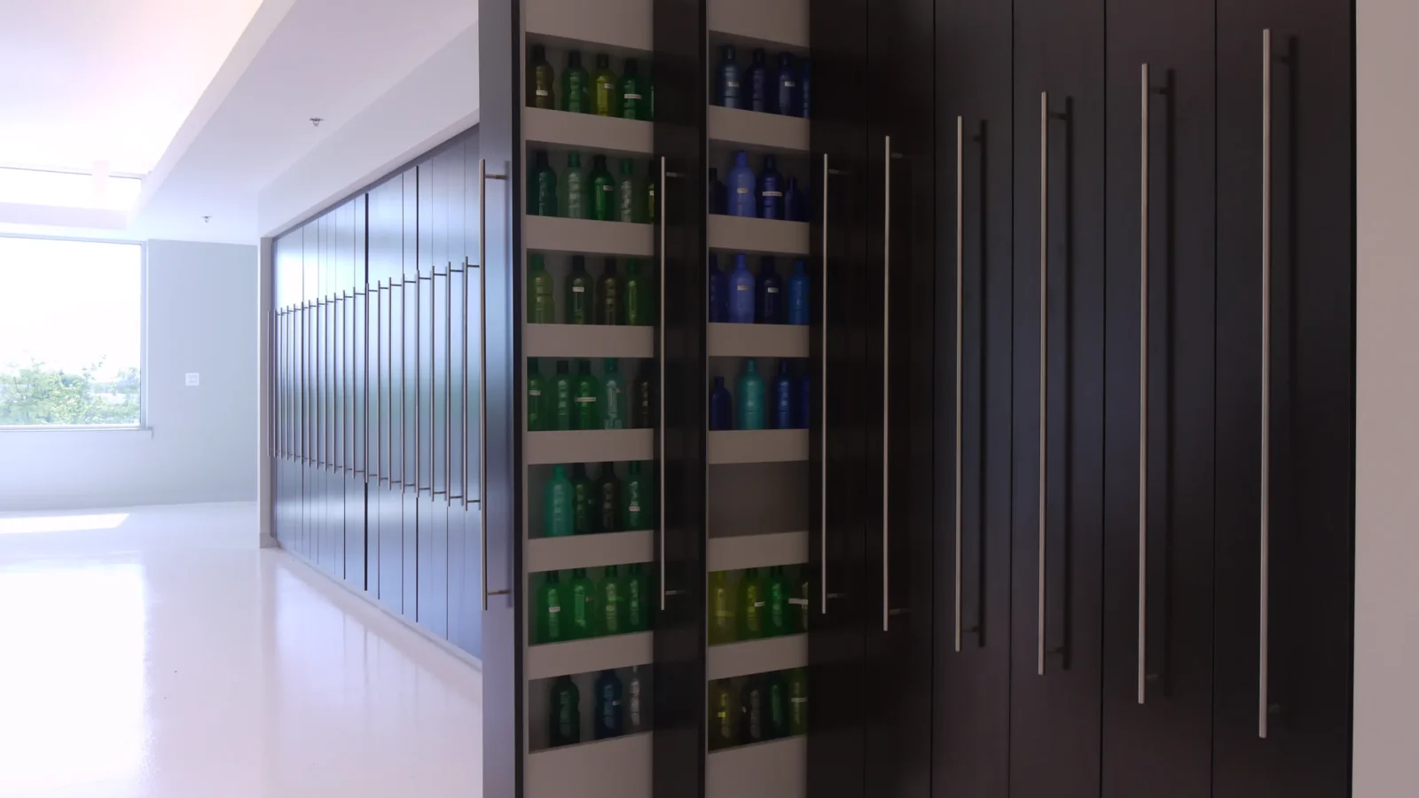 Full-height dark wood pull-out cabinets opened to reveal shelves of colored plastic bottle samples along the studio wall.
