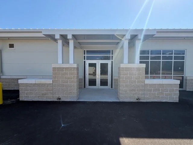 The entry of the Eglin AFB test facility: a white canopy on block piers over a pair of glass doors and a glazed storefront.