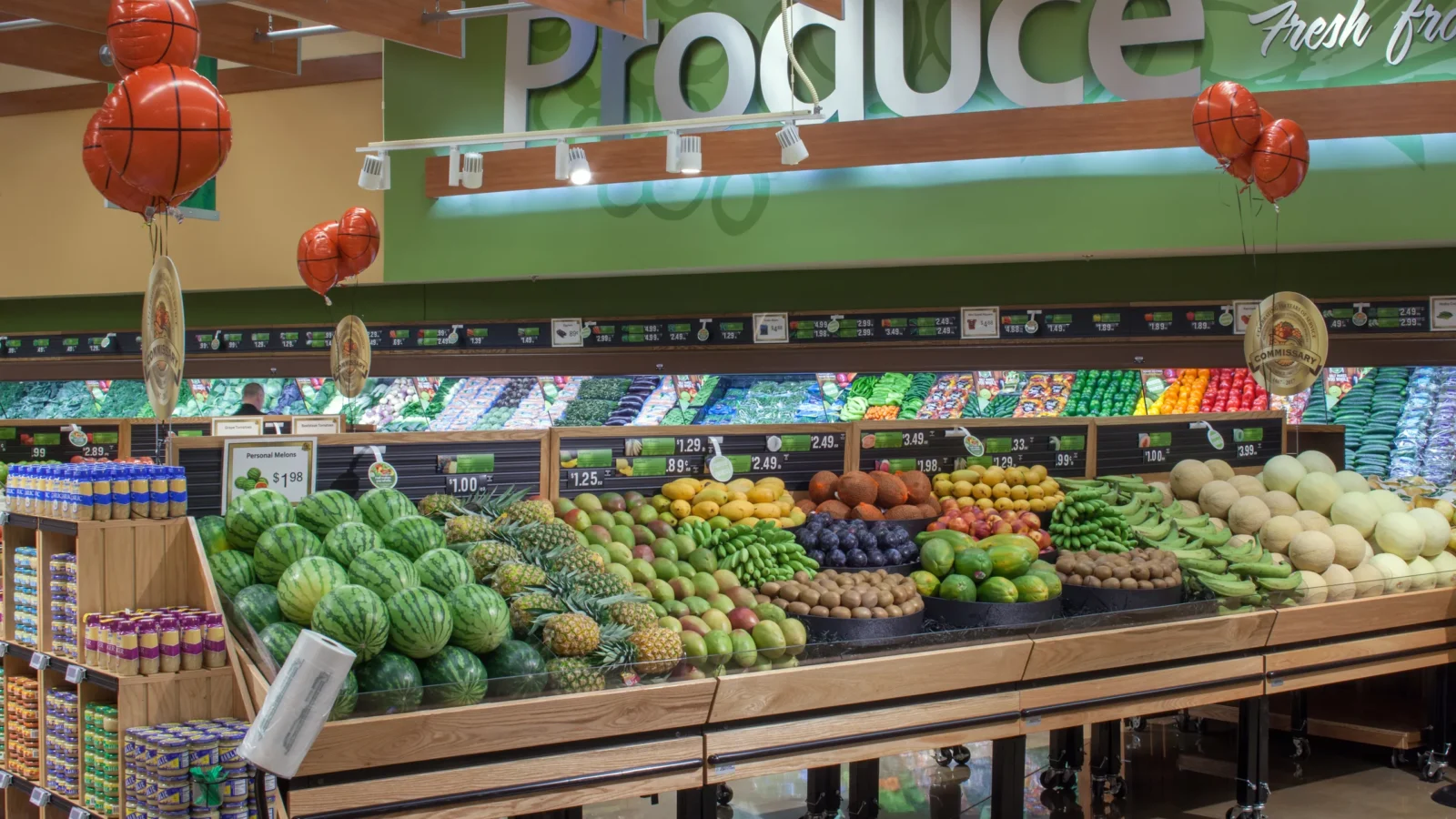 The produce department: green Produce signage over rows of wooden display tables stacked with fruit and vegetables.