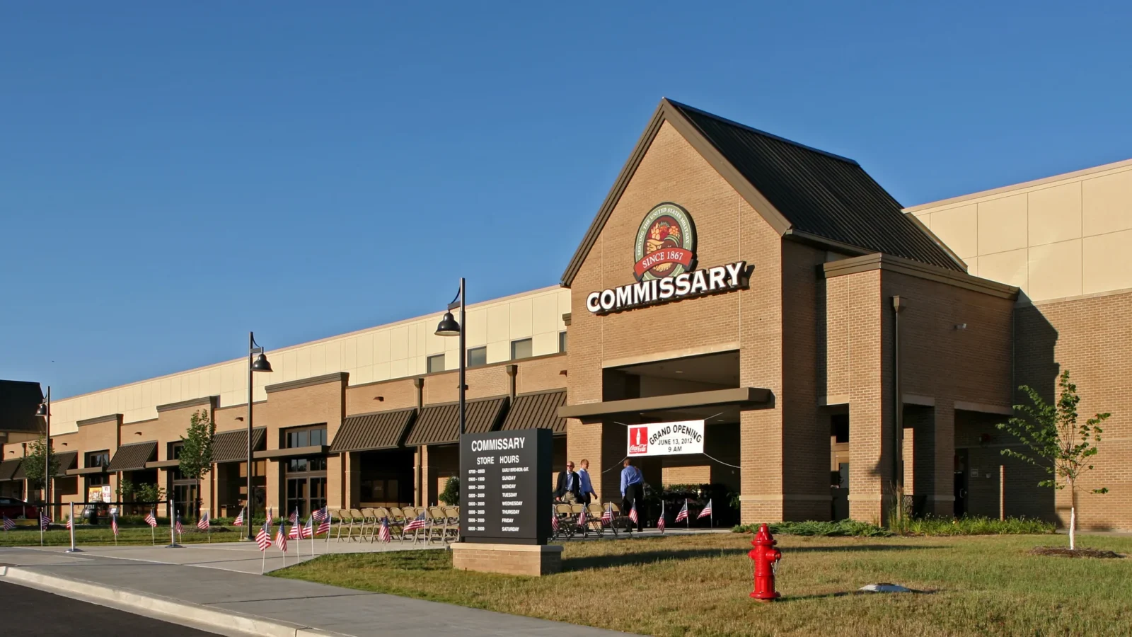Fort Campbell Commissary storefront with its brick gabled entry, DeCA emblem and Commissary sign, flags lining the walk on grand opening day.