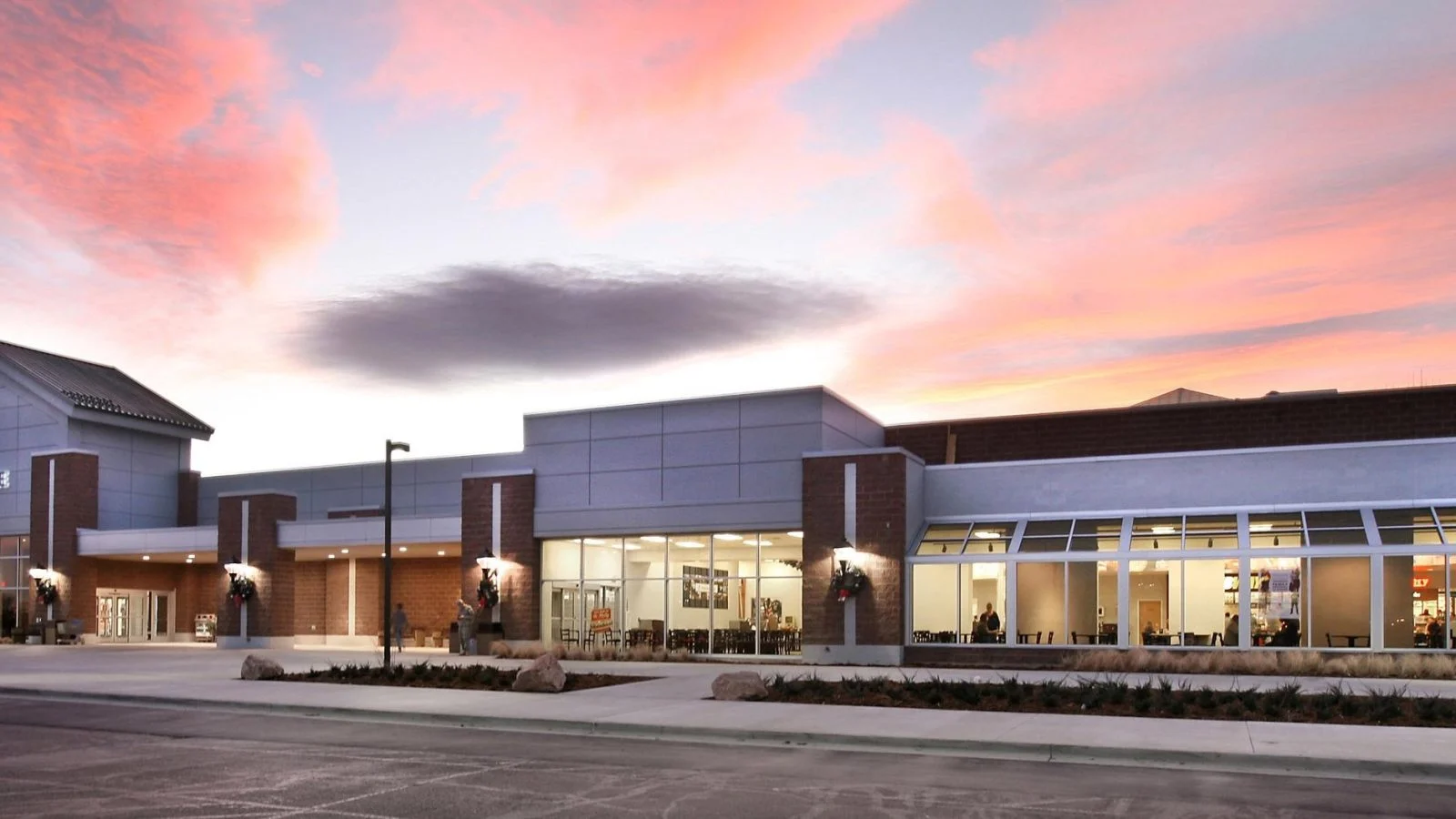 The Fort Carson Exchange at dusk — the full storefront under a pink sunset sky, with the gabled Exchange entry at left and a lit, glazed retail frontage running to the right.