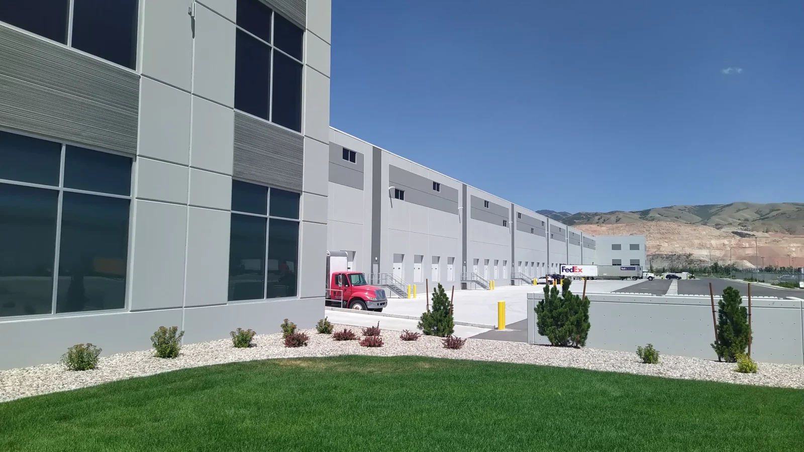 Truck court along the warehouse's dock doors, with a trailer at the docks and the Wasatch foothills beyond the landscaped berm.
