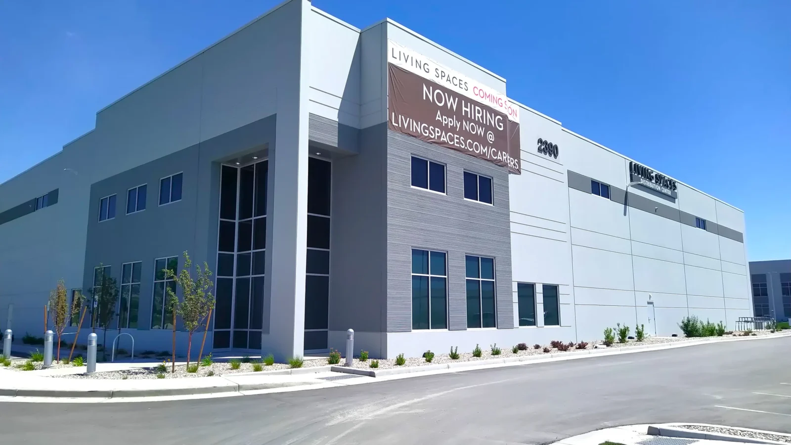 Corner of a second building in the center, with a tall glazed entry, textured grey panel bands and Living Spaces tenant signage.