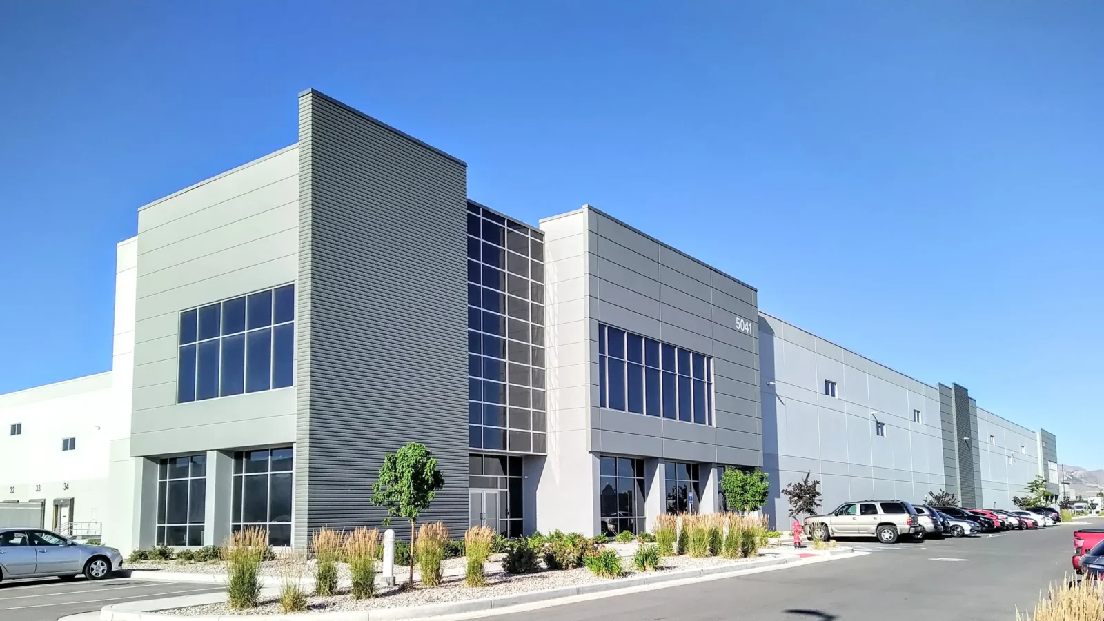 Lake Park 2's office front at 5041, with a dark corrugated fin, stacked curtain wall and grey tilt-up panels over landscaped parking.
