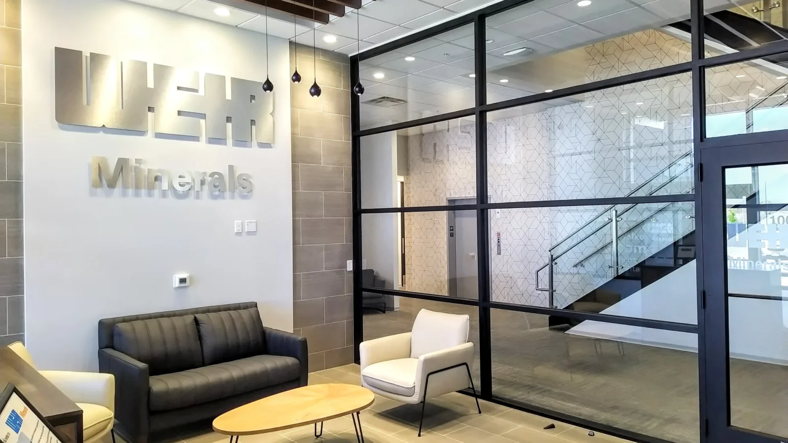 Weir Minerals lobby with dimensional wall lettering, lounge seating, a wood slat ceiling and a black-framed glass wall to the stair.