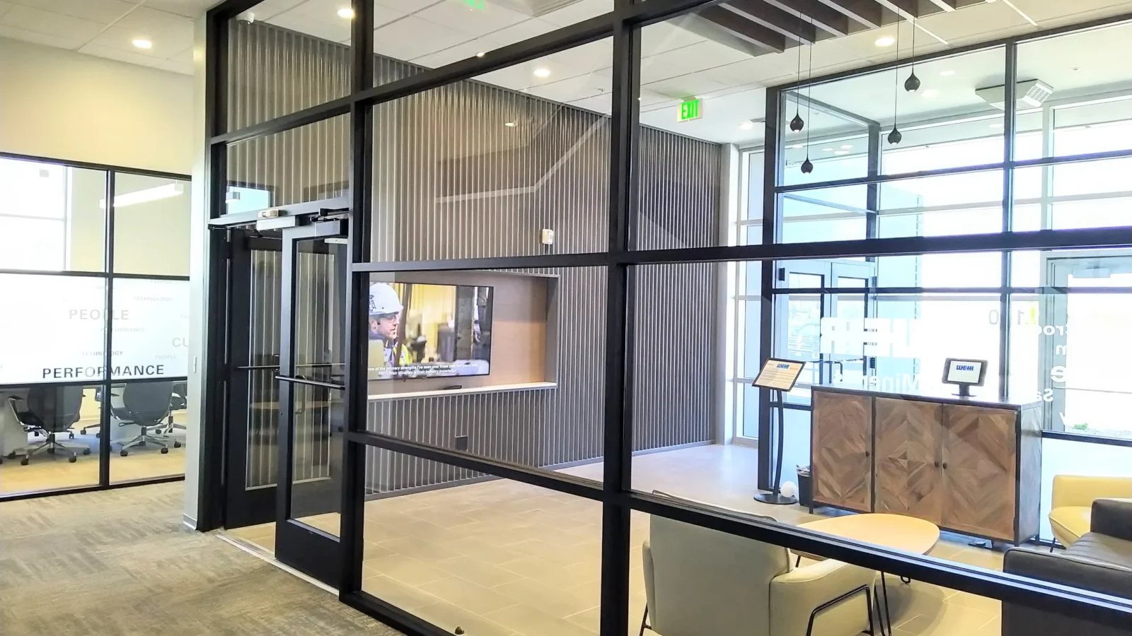 Black-framed glass vestibule opening to the reception area, with a slatted feature wall, display screen and a conference room beyond.