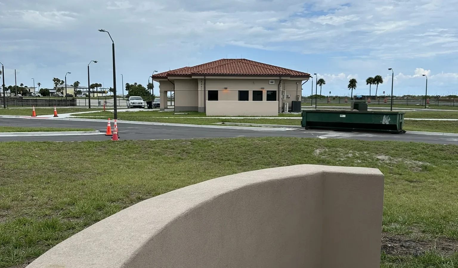 A curved stucco barrier wall at the edge of the gate complex, with the tile-roofed gatehouse across the lawn.