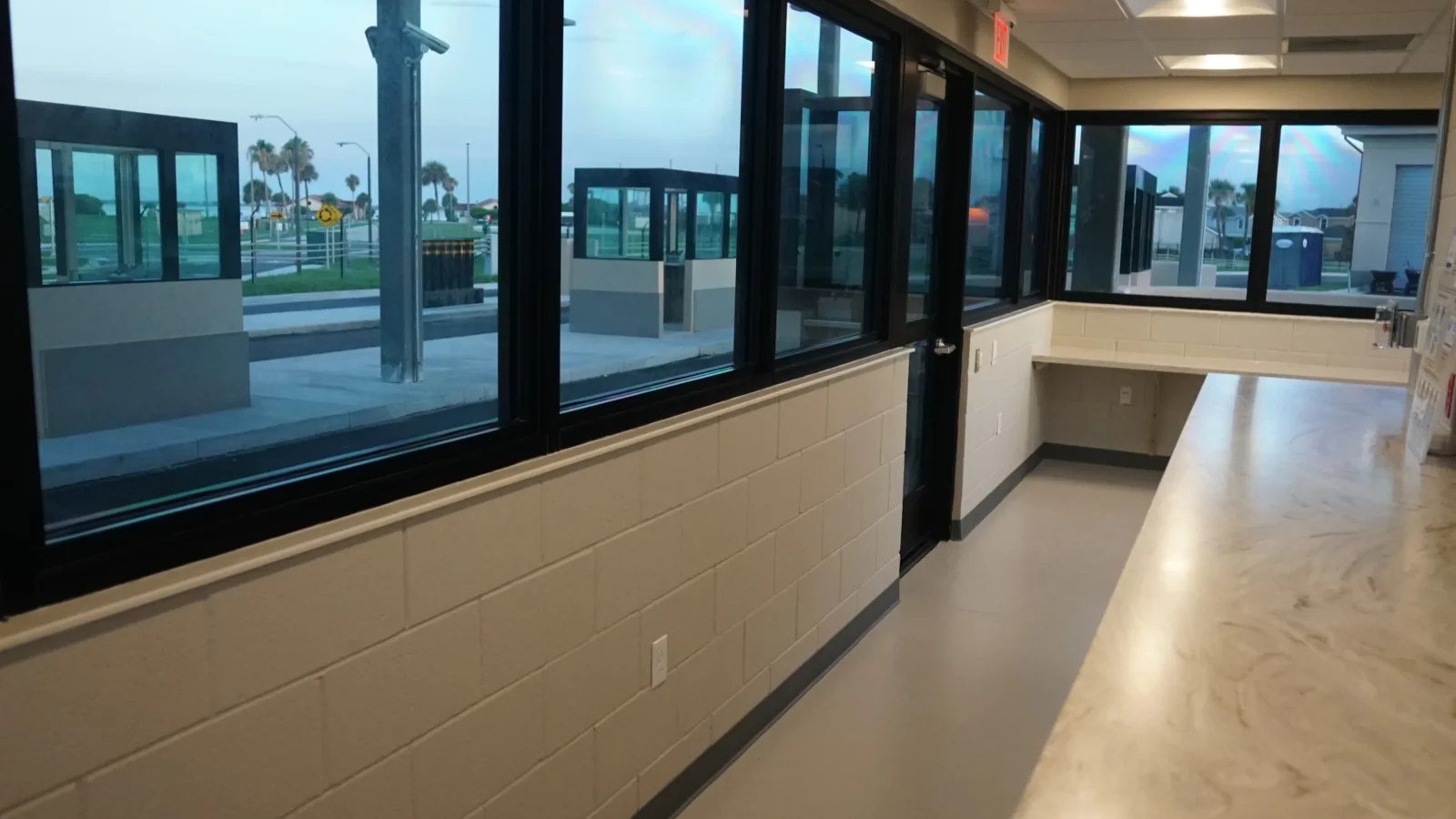 Inside the gatehouse: a long solid-surface counter beneath continuous windows looking out to the guard booths and canopy.