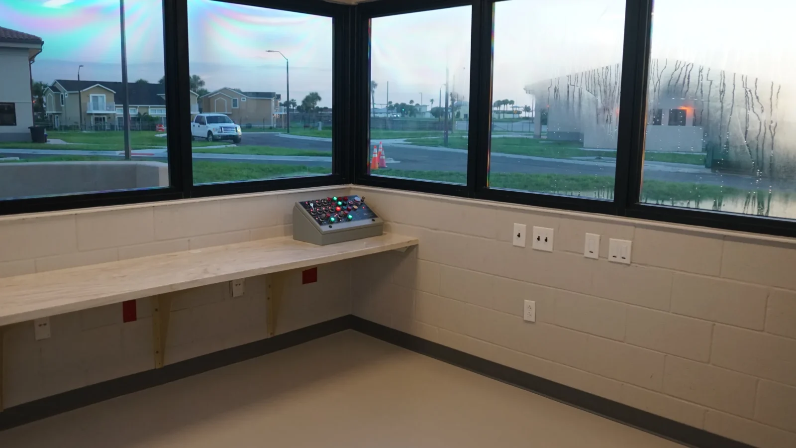 The gatehouse workstation: a wall-mounted counter and control panel beneath a corner run of windows.