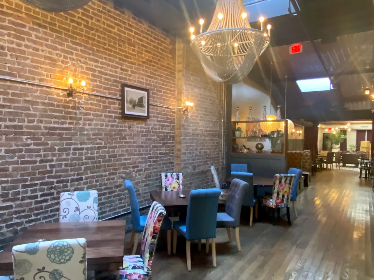 Pennyville Barcar ΓÇô Expansion & Remodel: the Pennyville dining room along the exposed-brick party wall, with a beaded chandelier, sconces and blue upholstered chairs.