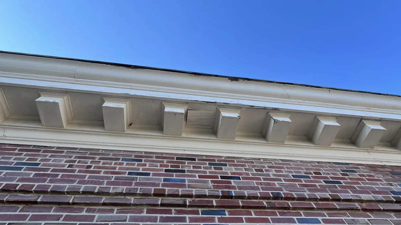 The NETC administration building's white dentil cornice above brick walls and double-hung windows, surveyed for the Package 4 window replacement.