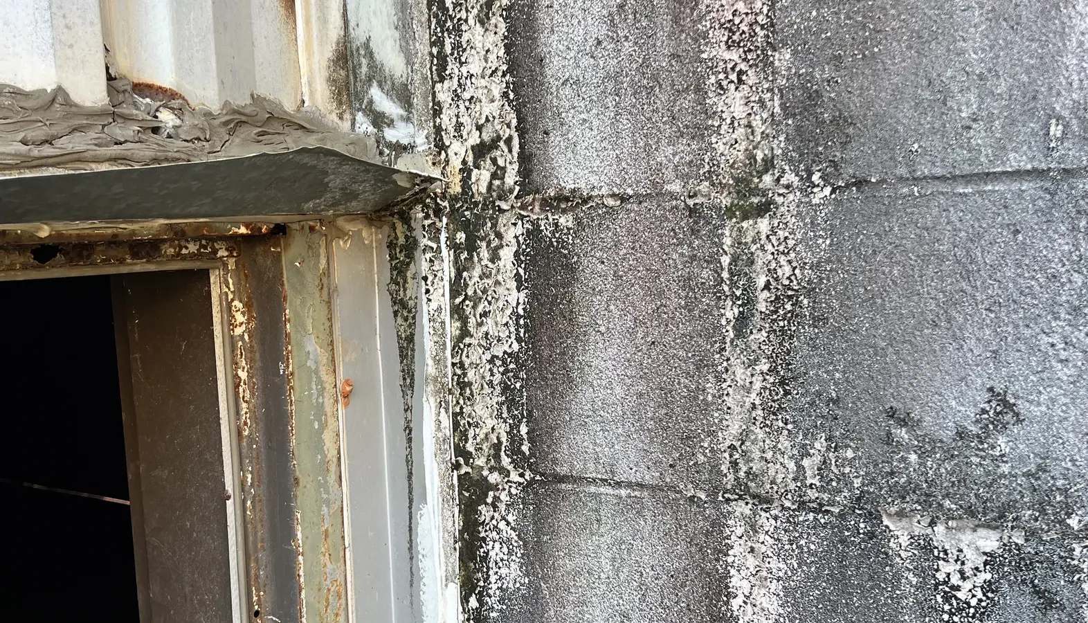 Storm-damaged metal wall panels and a corroded door frame at a relief supply storage building at NAS Pensacola.