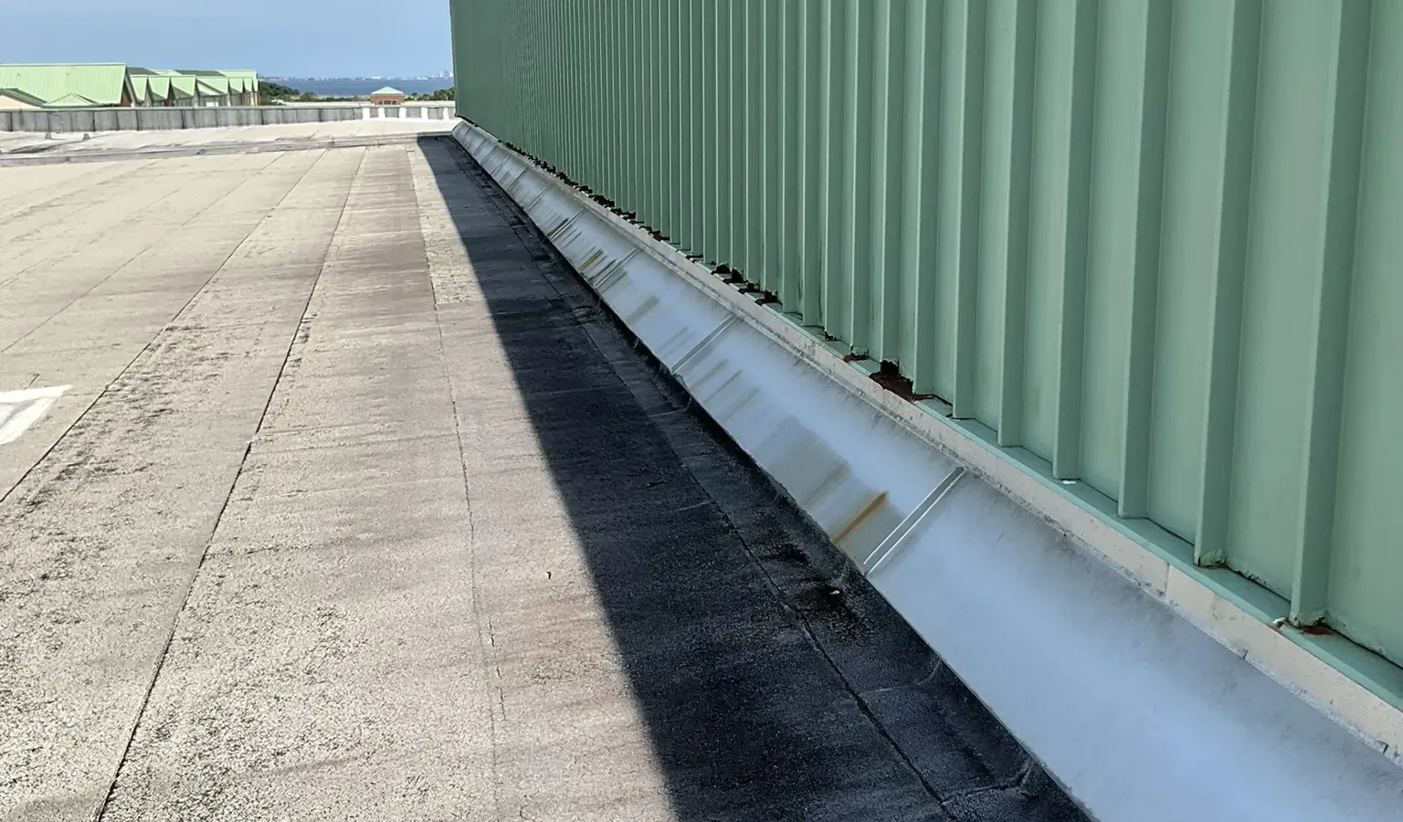 The green metal high-bay wall and low-slope roof of the Aviation Maintenance School at NAS Pensacola.