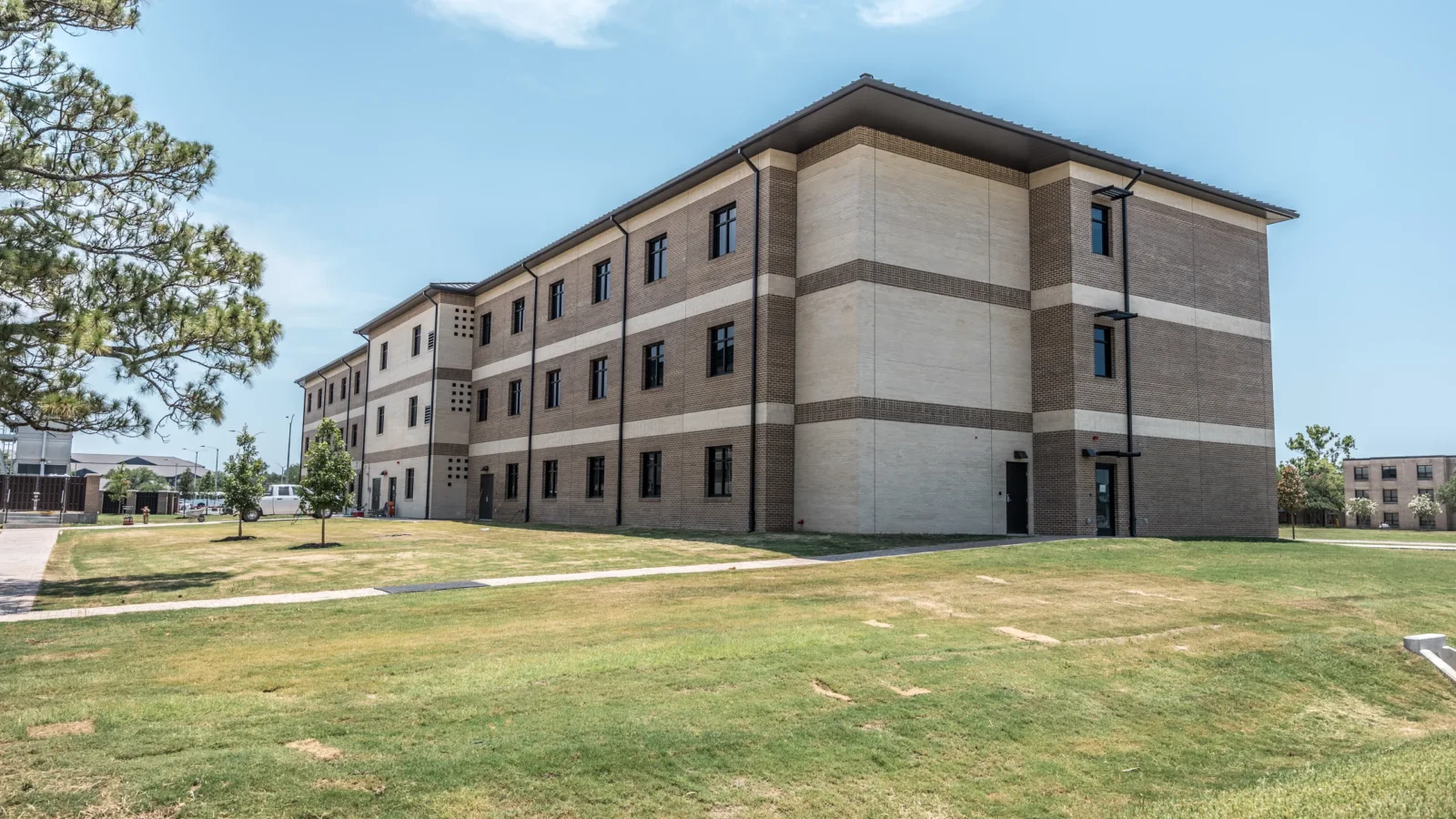 Residence Hall P855 at NCBC Gulfport, a three-story residence hall of cream architectural precast and banded brown brick under a standing-seam roof.