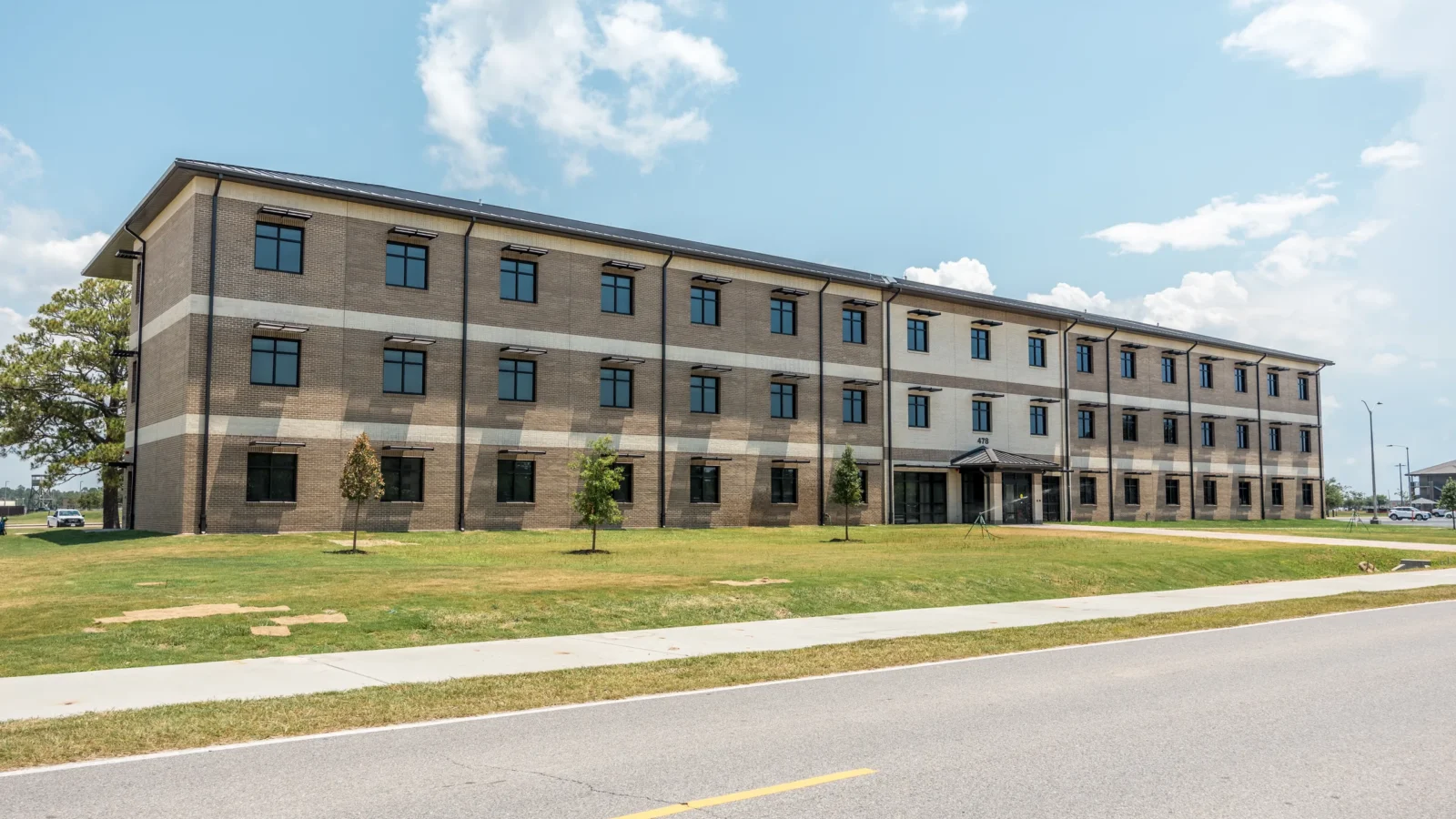 Long front elevation with alternating brick and precast bands, sunshades over the windows and a canopied main entry at the center.