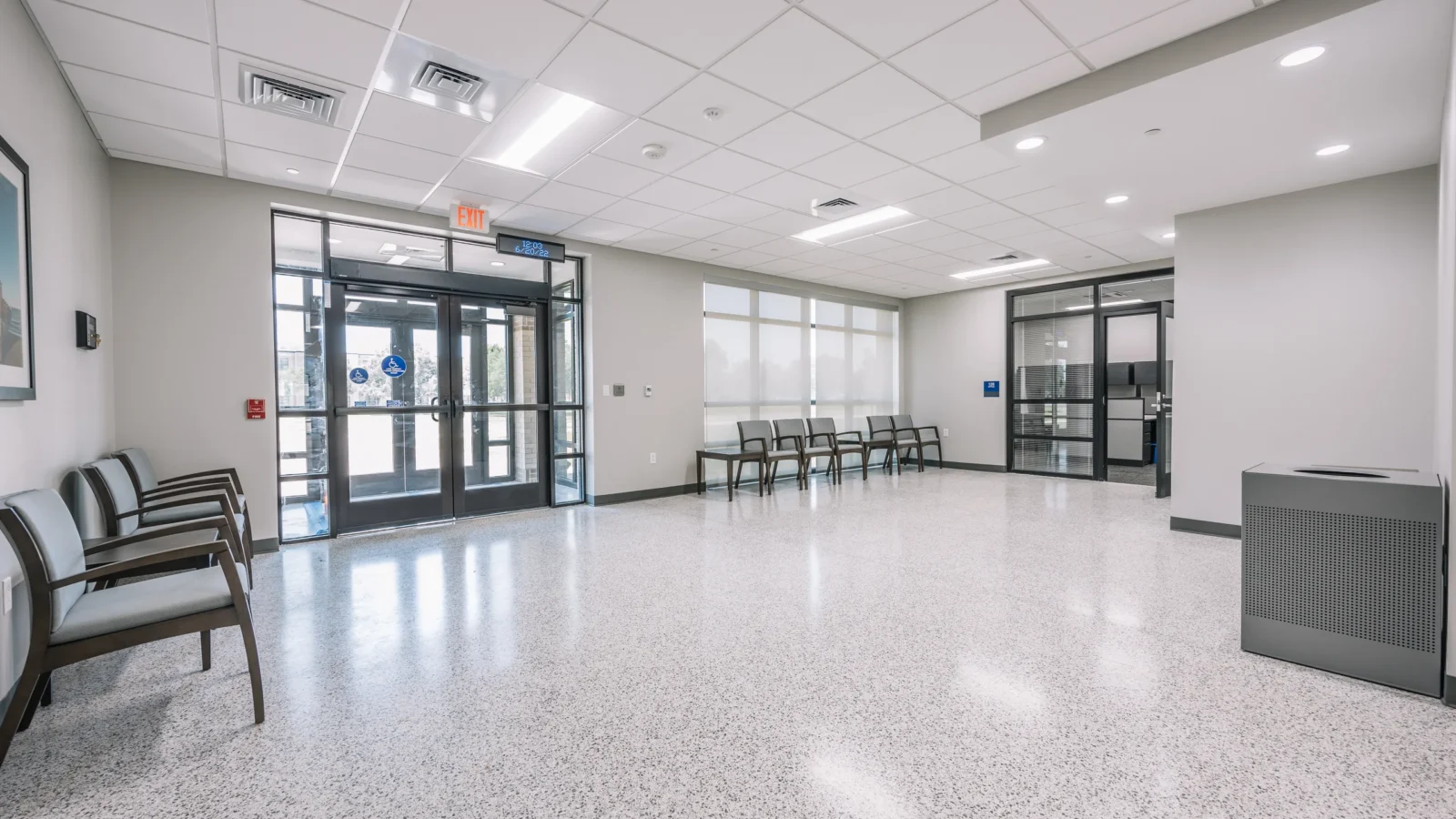 Entry lobby with a polished terrazzo floor, storefront doors, a daylit seating area and glass-walled offices beyond.