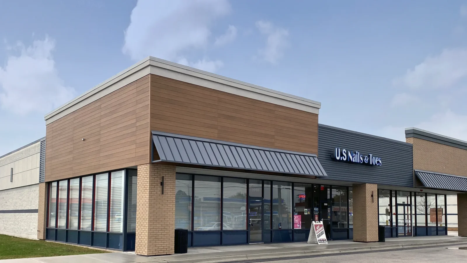 Retail Remodels at Chicago Ridge: a remodeled storefront building with wood-look cladding, tan brick piers, standing-seam metal awnings and full glazing.