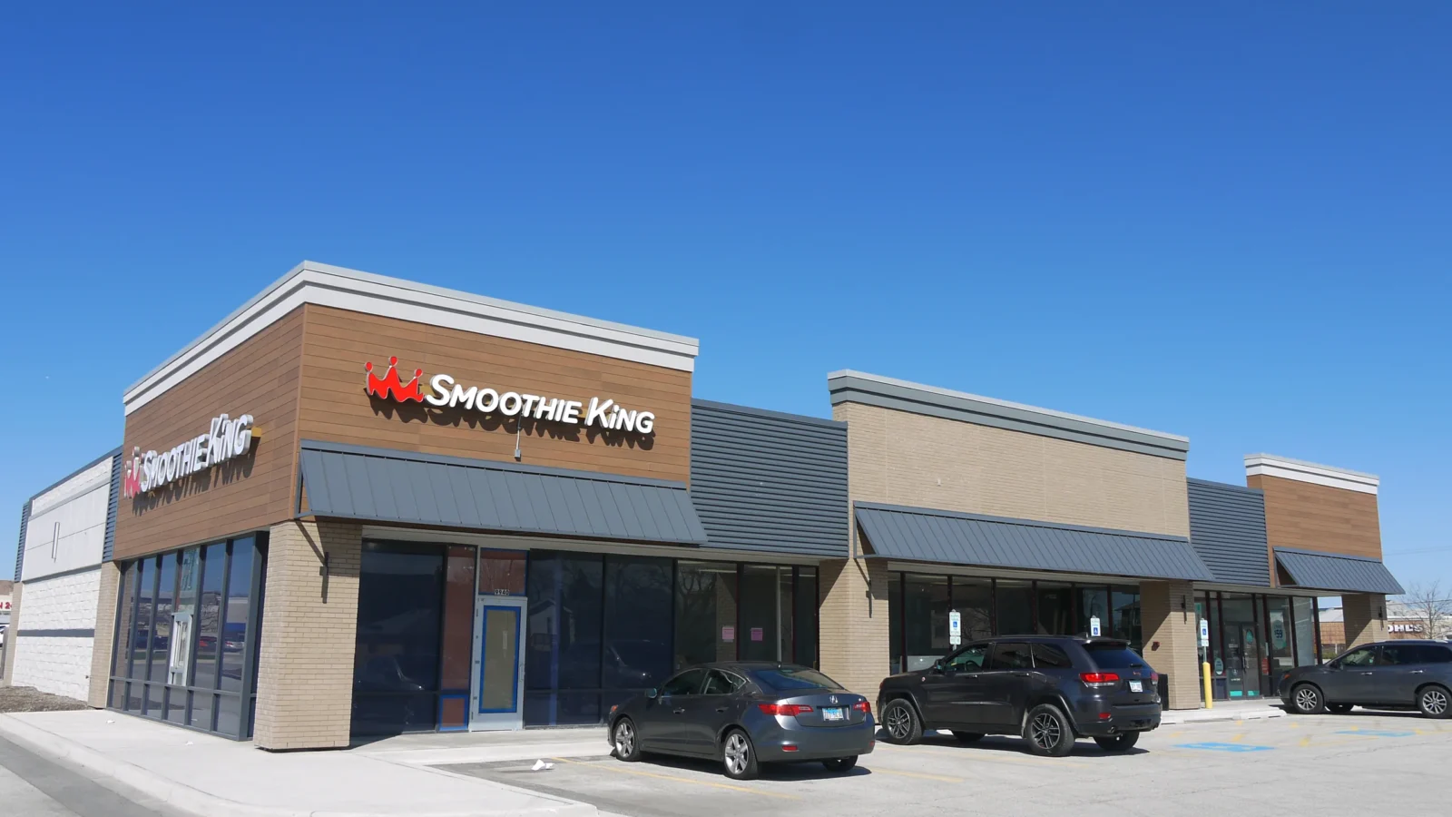 Remodeled corner retail building with Smoothie King signage on wood-look panels above dark metal awnings and tan brick piers.