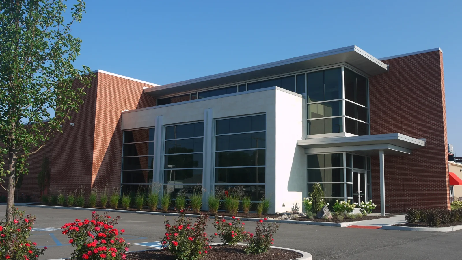 Strack & Van Til Corporate Office's new facade of red brick, cream stone and tall glazing under a thin projecting metal roof, with rose beds in front.
