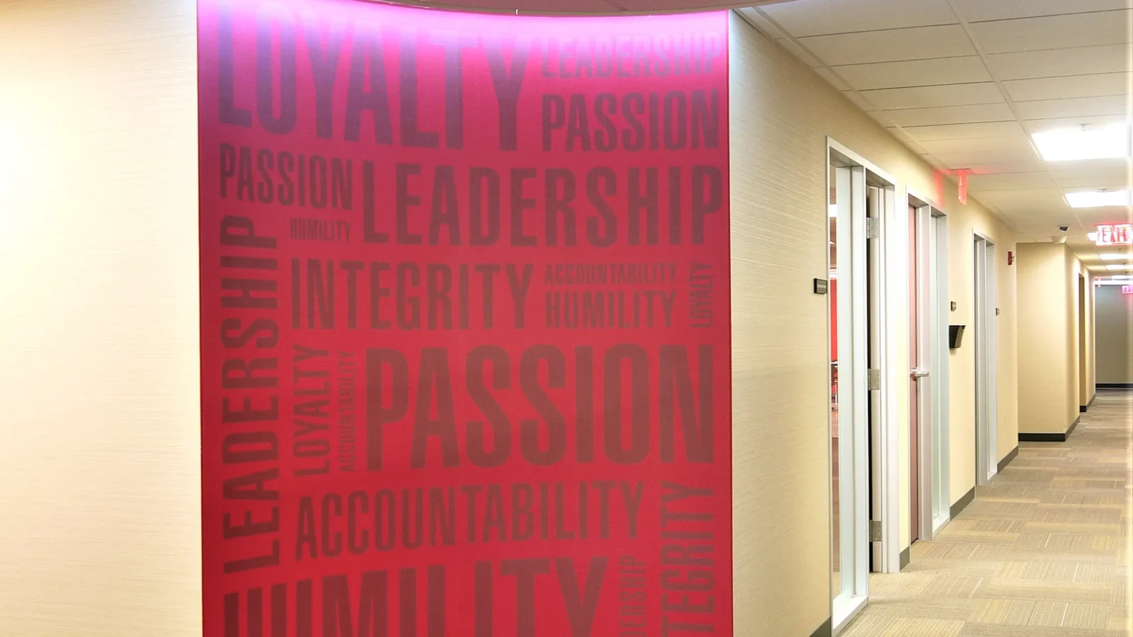 Curved red corridor wall printed with company values such as Loyalty and Passion, lit by a ring cove light over a round carpet inlay.