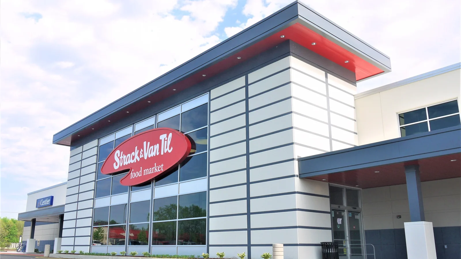 Strack & Van Til Grocery in Cedar Lake: banded precast storefront with a red-soffit roof, glazed corner and oval Strack & Van Til food market sign.