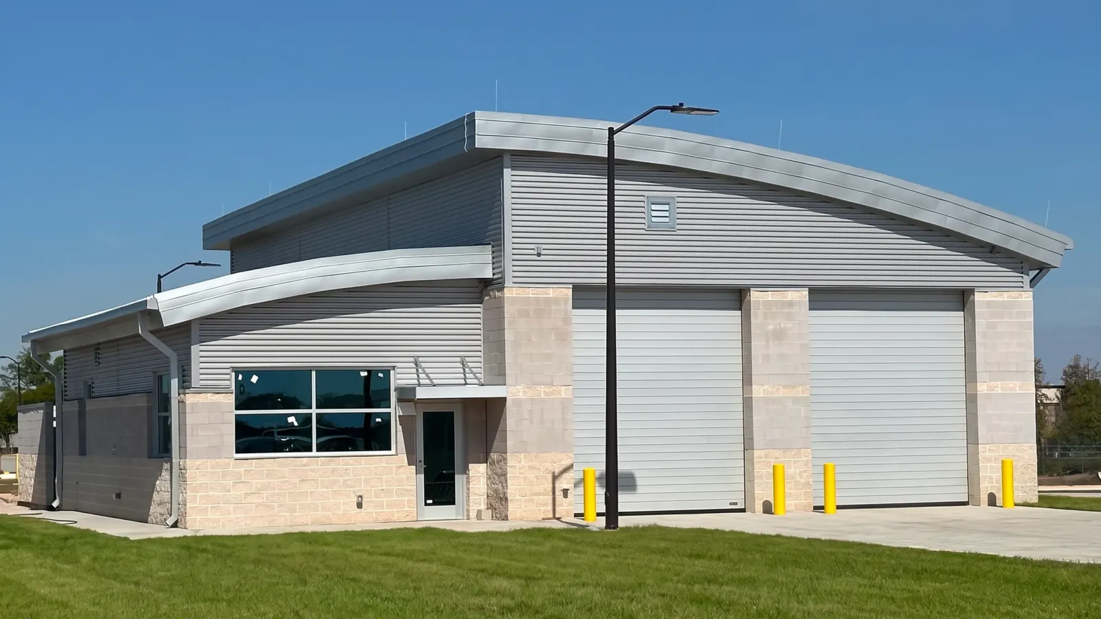 The vehicle inspection building at the Tyndall AFB commercial gate: split-face block below metal panel siding, two tall overhead doors and a curved standing-seam metal roof.