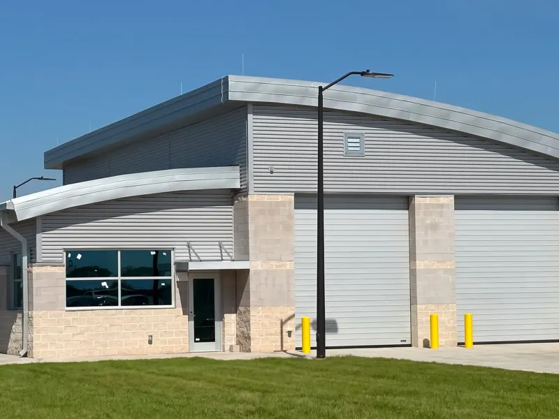 The vehicle inspection building at the Tyndall AFB commercial gate: split-face block below metal panel siding, two tall overhead doors and a curved standing-seam metal roof.