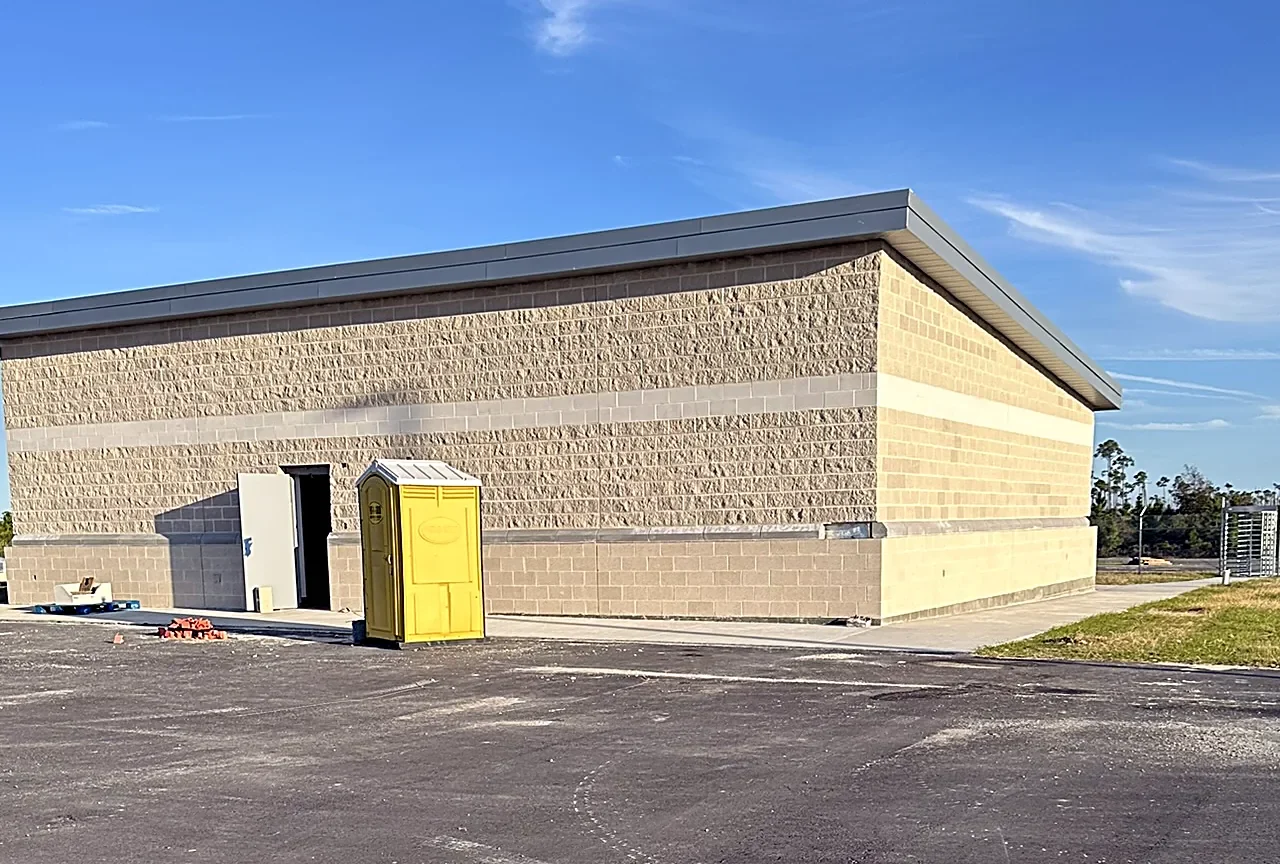 Tyndall AFB Munitions Storage Facility: split-face block walls with a smooth-block band and metal roof edge, photographed near completion across a new asphalt apron.