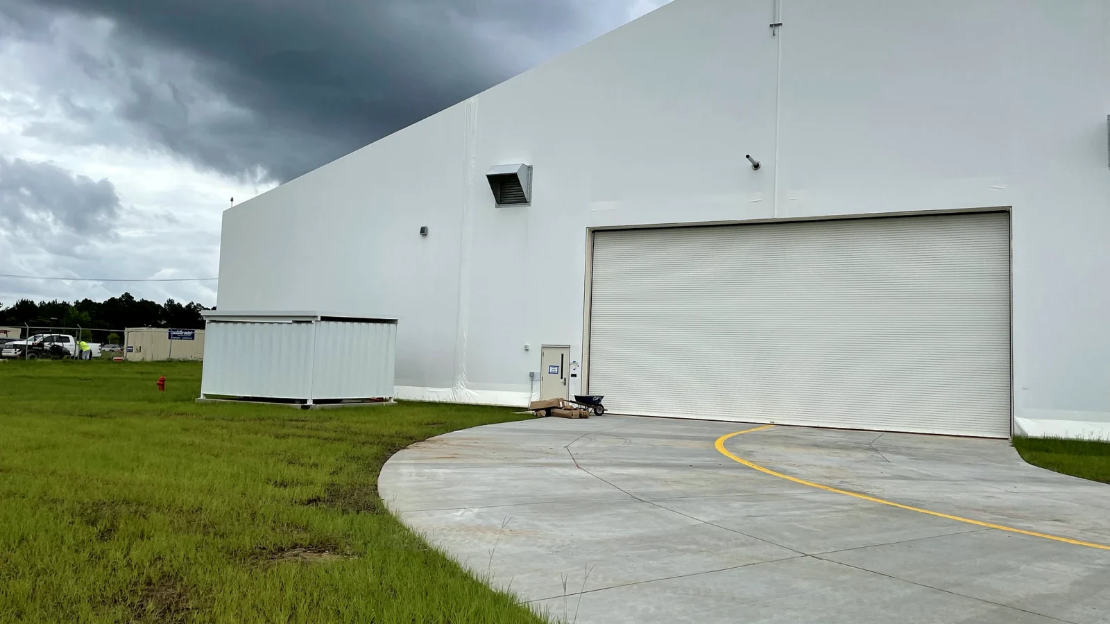 Whiting Field Maintenance Hangar: the finished hangar's white membrane-clad end wall and wide aircraft door, with the new concrete apron curving up to it under a stormy sky.