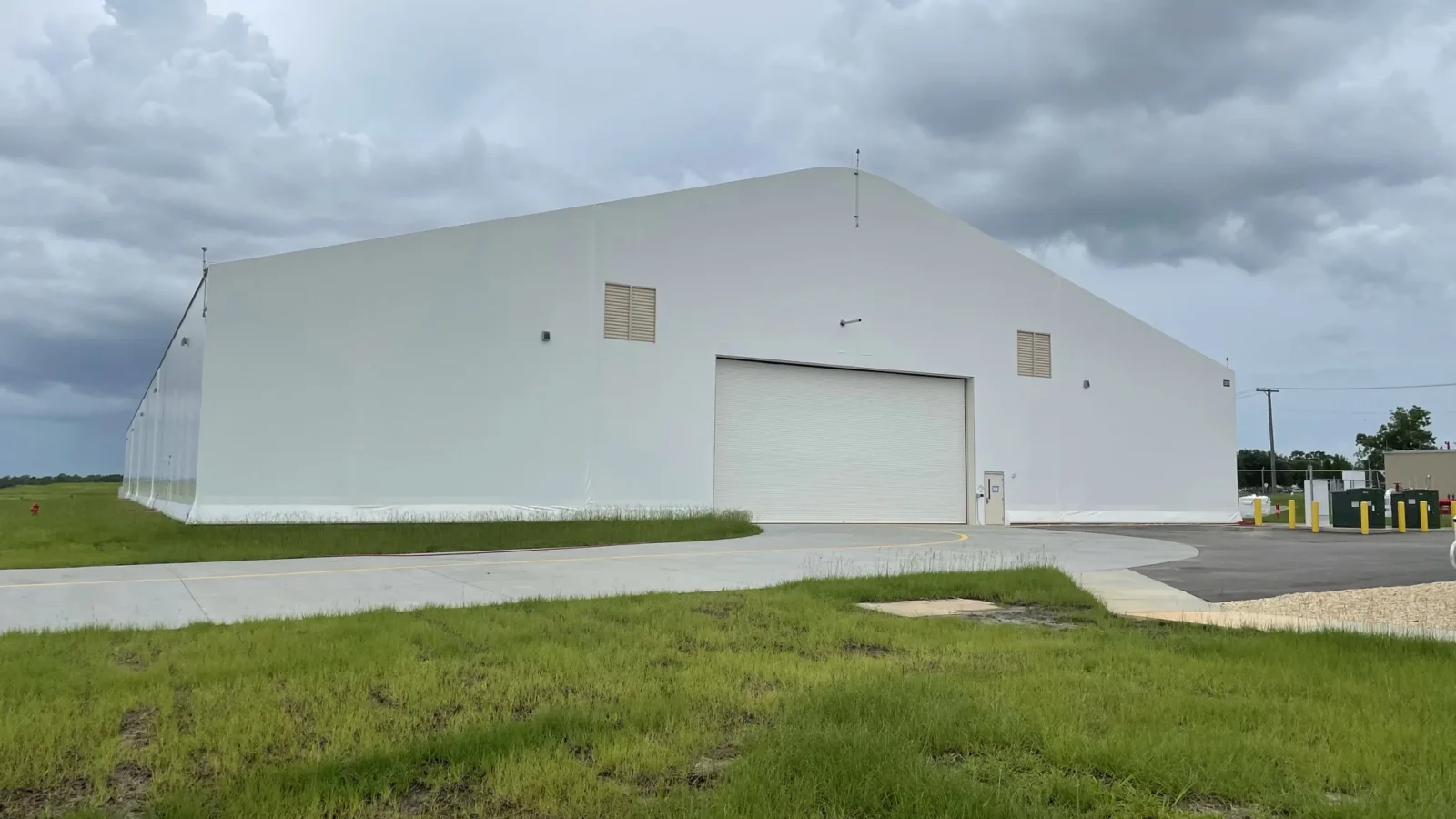 Whiting Field Maintenance Hangar: the full side elevation seen across the grass, its aircraft door set into the long white membrane-clad wall under a stormy sky.