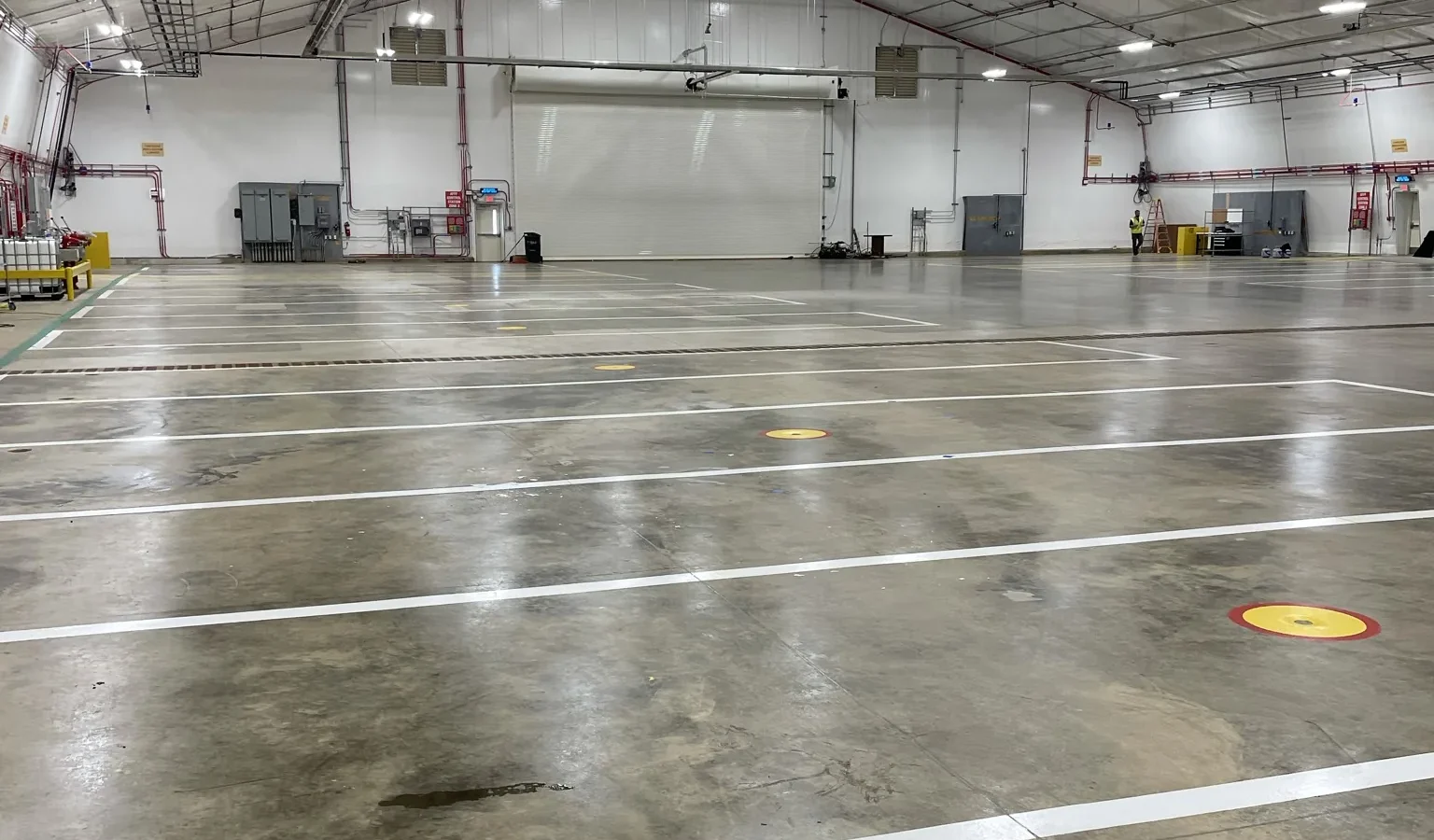 Inside the hangar: the empty clear-span aircraft bay, its polished concrete floor marked out with white bay lines and yellow and red floor markers, running to the aircraft door at the far end.