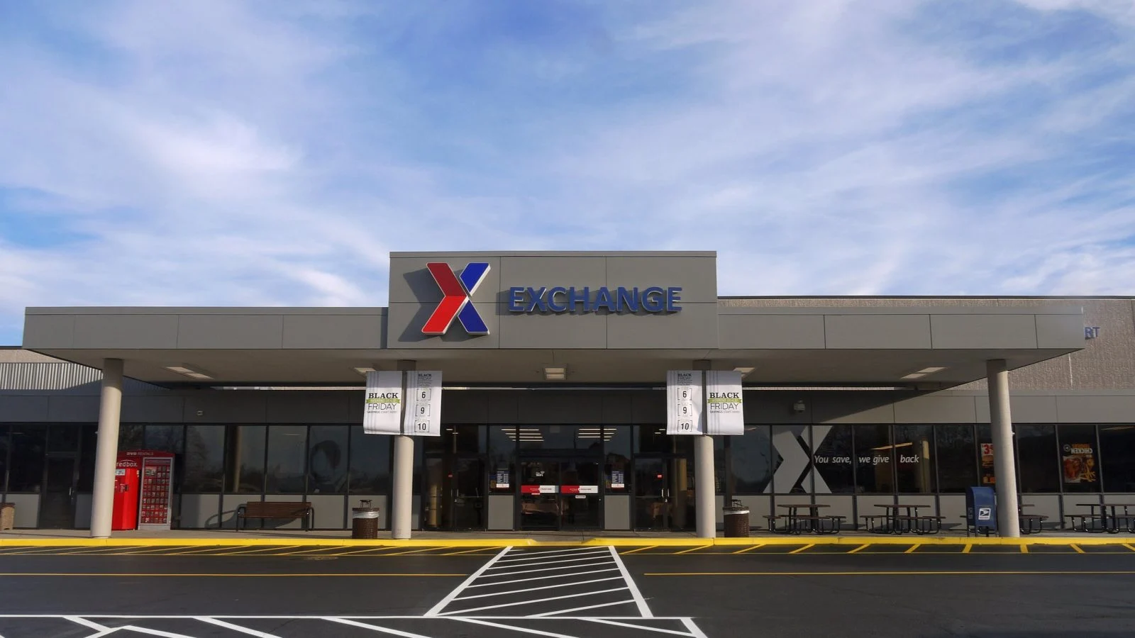 The Wright-Patterson Exchange main entry under a clear blue sky — a symmetrical canopy on slender columns fronting the glazed entrance, with the AAFES X mark and EXCHANGE sign above.